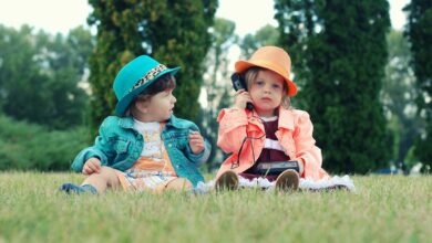 Two toddlers in colorful outfits enjoying playtime with walkie talkies in a sunny park setting.